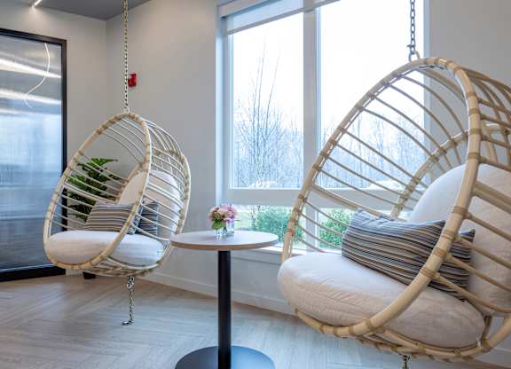 Two hanging wicker chairs with cushions and a small table with a vase of flowers at Seacoast Residences Apartments, Maine, 03904
