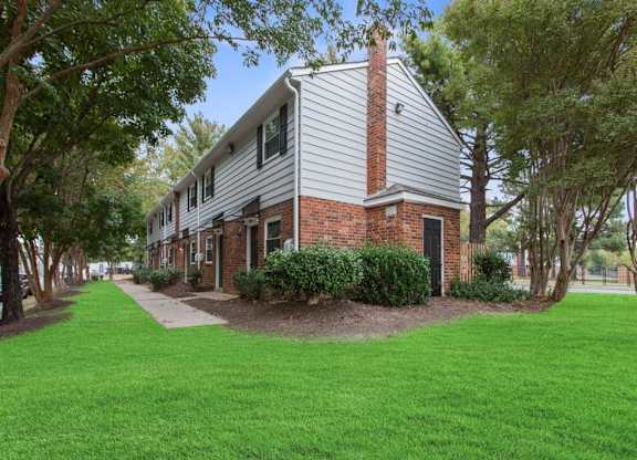 a white building with a brick chimney and green grass in front of it at The Lawton Townhomes, Virginia, 23832
