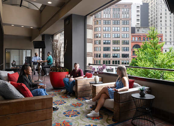 people sit on couches and chairs in a lobby with a large window