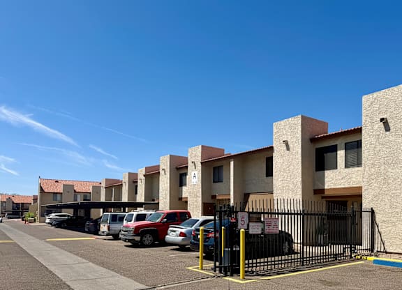 A parking lot with cars and a gated entrance to apartment buildings.
