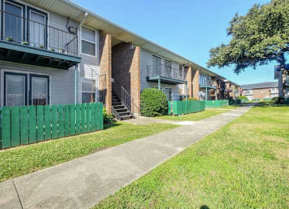 A row of apartment buildings with green fences and a sidewalk in front.