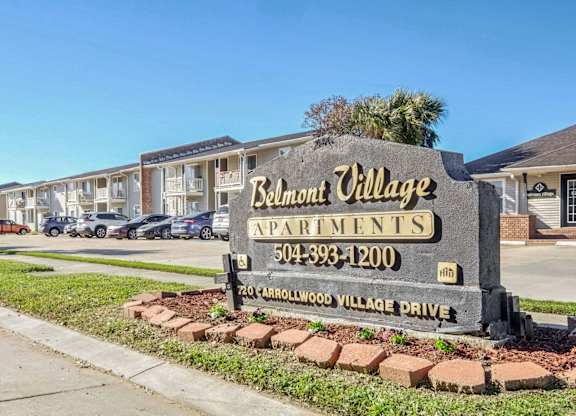 A sign for Belmont Village Apartments is in front of a row of houses.