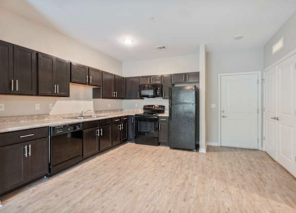 A kitchen with dark brown cabinets and a black fridge.