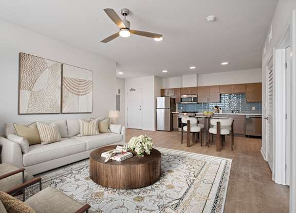 A modern living room with a white sofa, a wooden coffee table, and a dining area in the background.