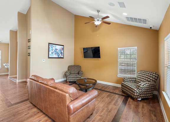 A living room with a brown leather couch and a flat screen TV mounted on the wall.