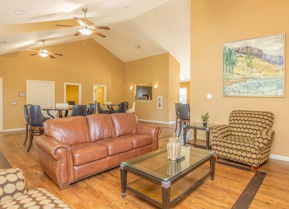 A living room with a brown leather couch, a glass coffee table, and a painting on the wall.