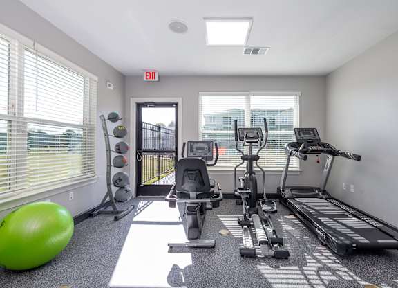 A well-equipped gym with treadmills, elliptical machines, and a green exercise ball.