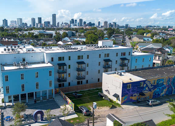 A blue and white building with a mural on the side is in the foreground with a city skyline in the background.