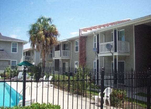 A pool is surrounded by a black fence and chairs are placed around it.