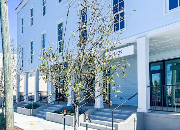 A tree in front of a white building with the number 1429 on it.