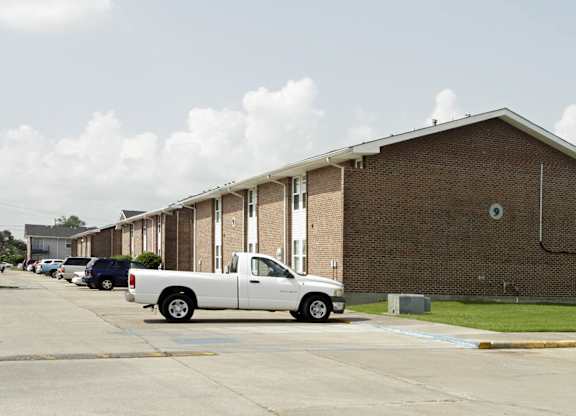 A white pickup truck is parked in a parking lot in front of a brick building.