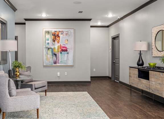 A modern living room with a grey armchair, a patterned rug, a wooden cabinet, and a large abstract painting on the wall.