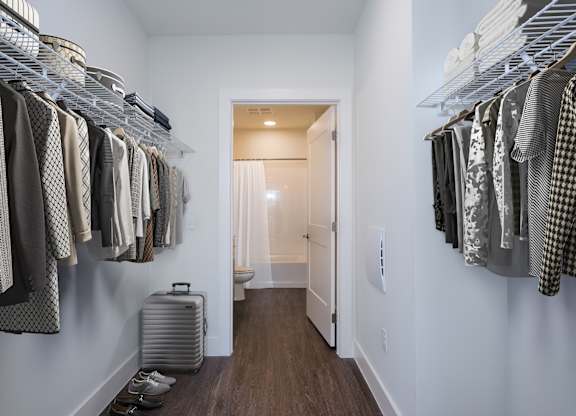 A hallway with clothes hanging on both sides and a suitcase on the floor.