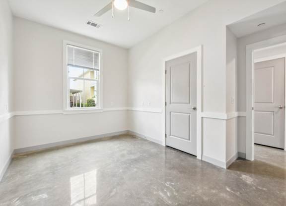 A room with a window, a ceiling fan, and two doors.