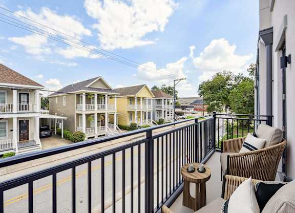 A balcony with a chair and a table overlooks a street with houses.
