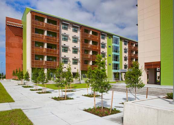 A modern building with a green and brown exterior and a courtyard with trees and grass.