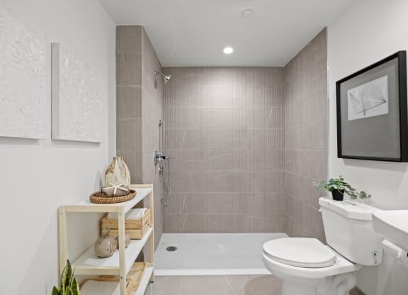 a bathroom with tiled walls and floor and a walk in shower with a glass door at The Fairfax Flats Apartments, Los Angeles, CA