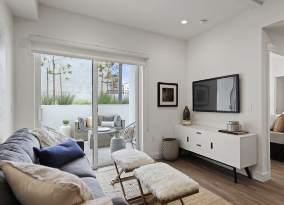 a living room with a couch and a tv in front of a sliding glass door at The Fairfax Flats Apartments, Los Angeles, CA