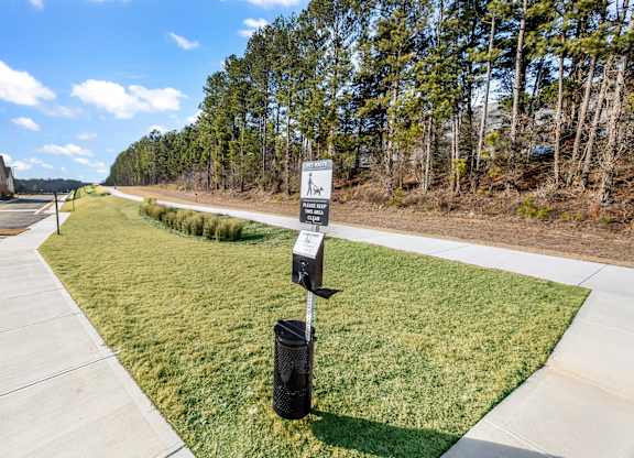A signpost with a walking person symbol stands on a grassy area next to a paved walkway.