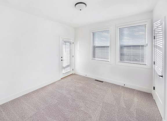 A room with a carpeted floor and two windows with blinds.