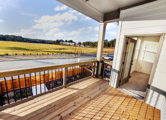 A wooden deck with a white house and a field in the background.