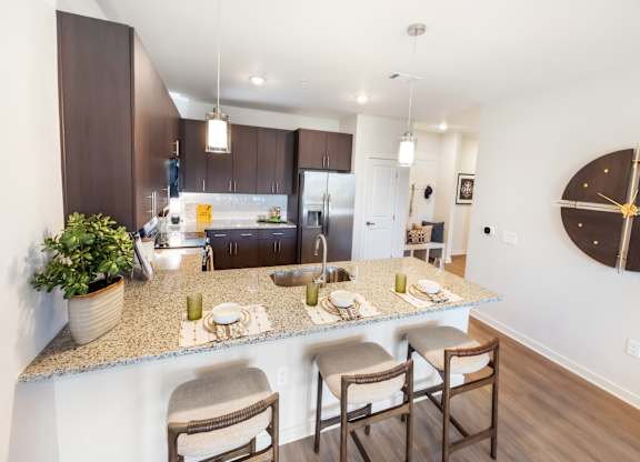 A kitchen with a counter and chairs in the foreground and a dining area in the background.