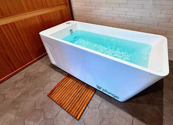 A white hot tub with a blue interior is on a tiled floor in a bathroom.
