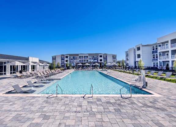 A large swimming pool surrounded by lounge chairs and buildings in the background.
