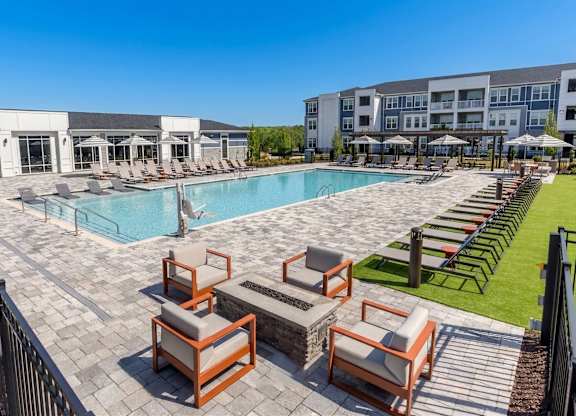 A pool surrounded by chairs and a building in the background.