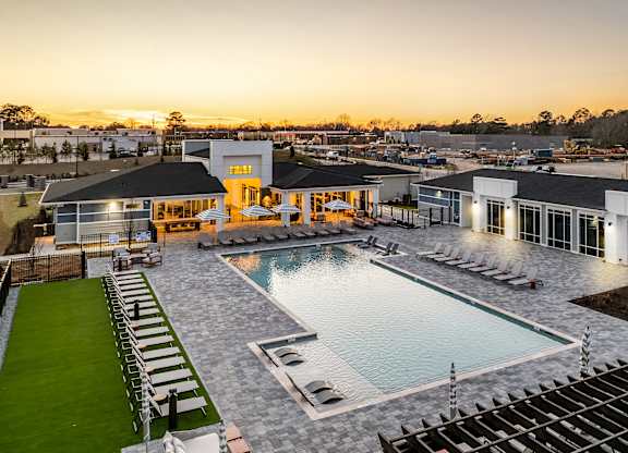 A large outdoor swimming pool surrounded by lounge chairs and a building with a yellow entrance.