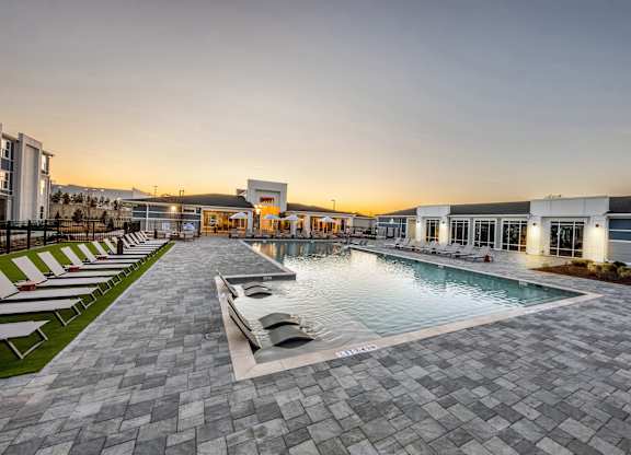 A swimming pool surrounded by a paved area and lounge chairs.