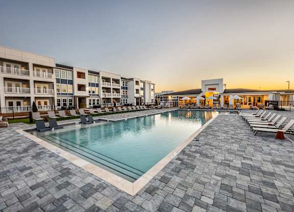 A large outdoor swimming pool surrounded by a stone patio and lounge chairs.
