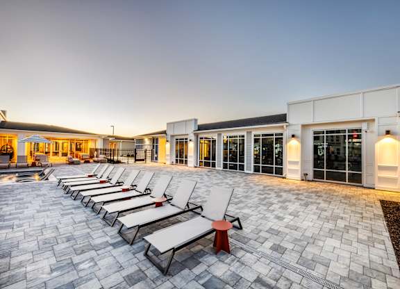 A row of lounge chairs are set up on a paved area outside a building.