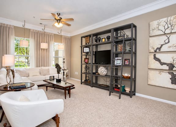 A living room with a white couch, a coffee table, a ceiling fan, and a large bookshelf.