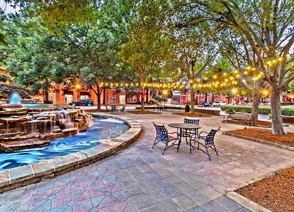 A beautiful outdoor area with a fountain, seating, and trees.