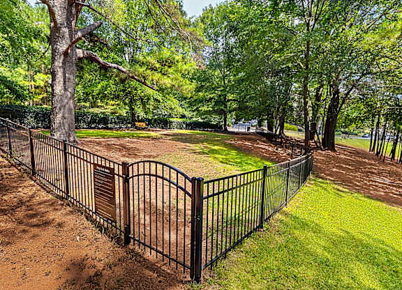 A black metal fence surrounds a dirt area with a tree in the background.