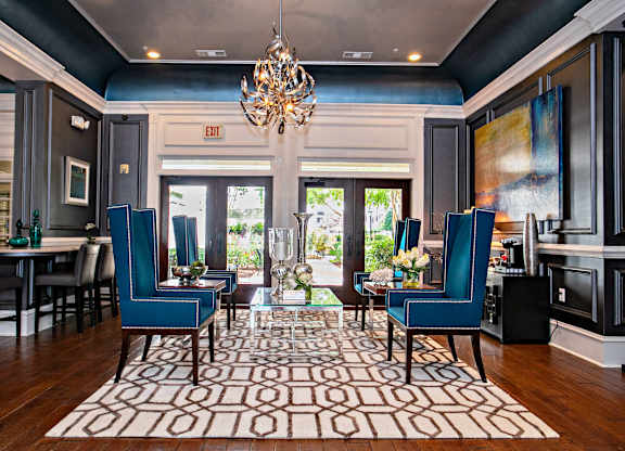 A living room with a chandelier, two blue chairs, and a patterned rug.