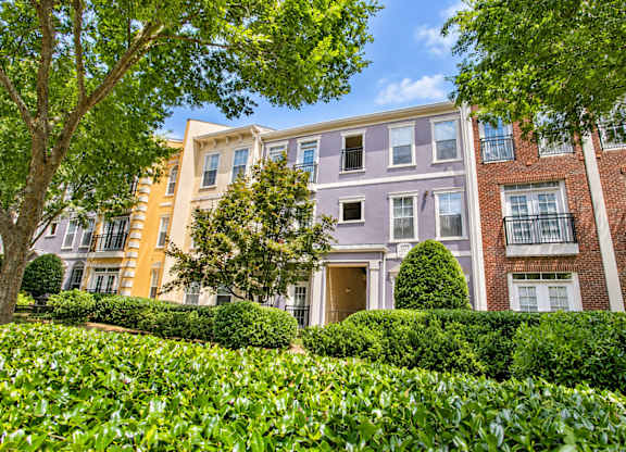 A row of apartment buildings with green bushes in front.
