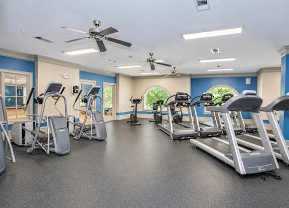 A spacious gym with treadmills, elliptical machines, and a fan.