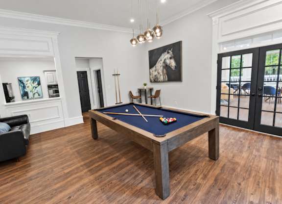 A pool table in a room with a leather chair and a painting of a horse on the wall.