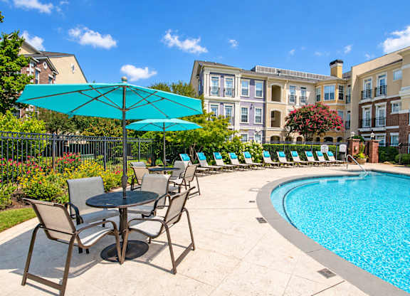 A pool area with chairs and umbrellas in front of a building.