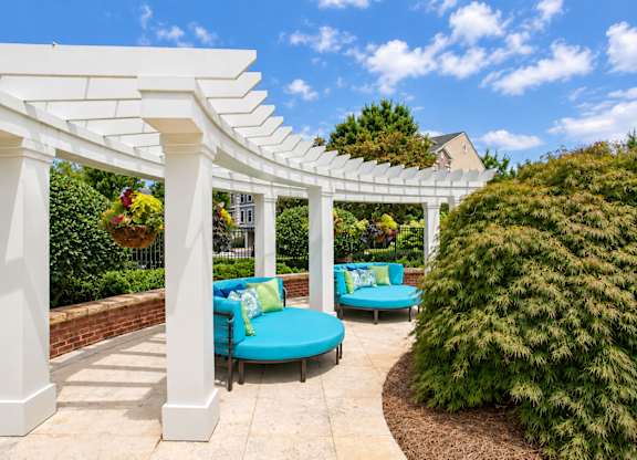 A white pergola with a blue cushioned bench underneath it.