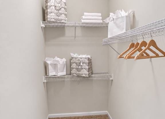 A white closet with a carpeted floor and shelves with clothes.