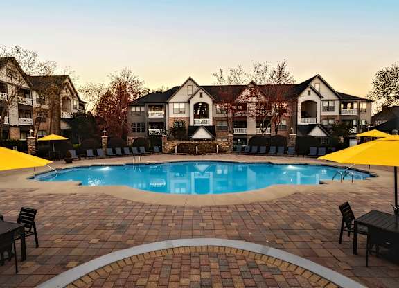 A large outdoor swimming pool surrounded by a brick patio and lounge chairs.