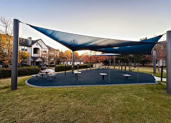 A playground with a blue shade structure and a round play area.