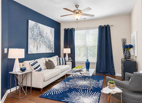 A living room with a white couch, a blue rug, and a ceiling fan.