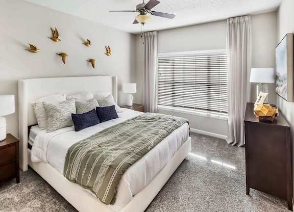 A bedroom with a large bed, a ceiling fan, and a wall decoration of birds.