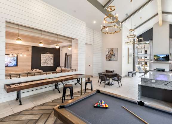 A pool table is in the middle of a room with a bar and a television.