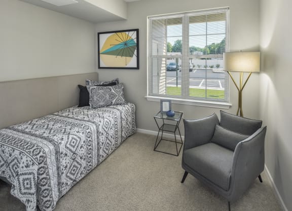 a bedroom with a bed and a chair and a window at Eden & Main 55+ Apartments, Southington, CT
