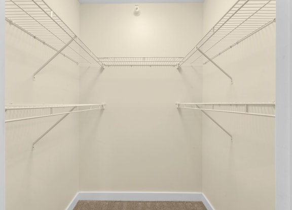 a spacious walk in closet in a home with white walls and empty shelves